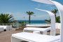 Terrazza con lettini bianchi, palme e vista sul mare.