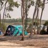 Una tenda verde con sedie da campeggio tra alberi vicino a un lago.