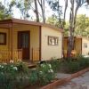 Bungalow gialli con terrazza accanto a un vialetto fiorito e alberato.