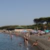 Spiaggia affollata con persone in costume, ombrelloni colorati e una struttura in lontananza.