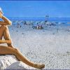 Una donna seduta su uno scoglio guarda il mare; ombrelloni chiusi sulla spiaggia.